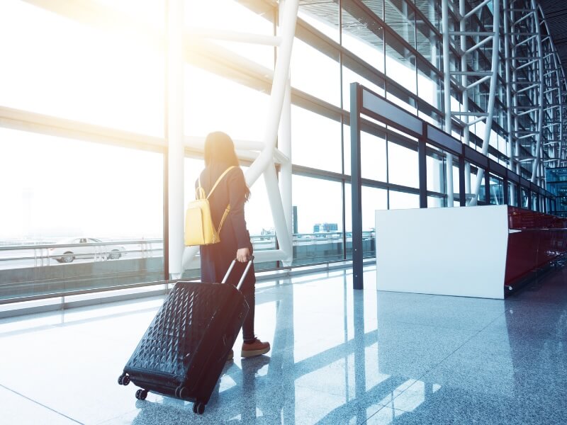 woman with yellow backpack and suitcase walking towards the gate at an airport
